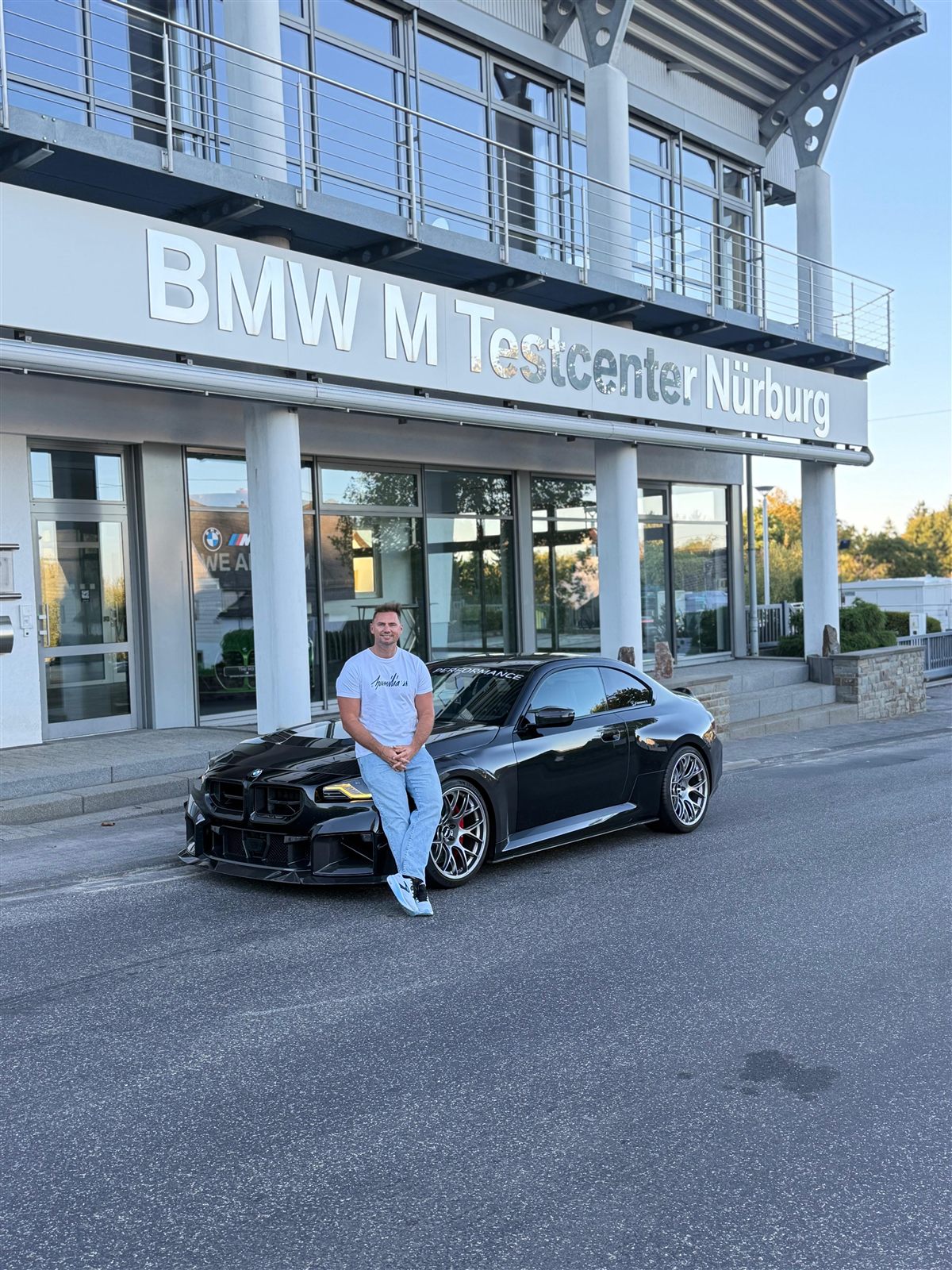Jannik Laessing, Inhaber von JL Performance, auf einem schwarzen BMW M2 vor dem BMW M Testcenter Nürburg